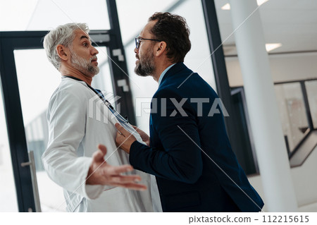 Violence against health workers. Patient is aggressive, have conflict with doctor in hospital corridor. Visitor holding doctor by coat, screaming, threatening him. Violence against health workers. Patient is aggressive, have conflict with doctor in hospital corridor. Visitor holding doctor by coat, screaming, threatening him. 112215615
