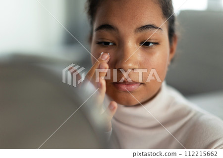 Portrait of beautiful curvy woman, looking at small round makeup mirror at home. 112215662