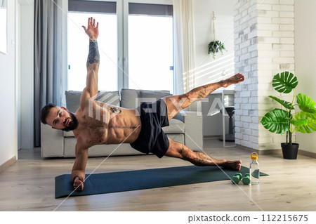 Handsome man doing yoga, stretching, resting after home workout, New Year's resolutions, exercising as healthy lifestyle and selfcare. Handsome man doing yoga, stretching, resting after home workout, New Year's resolutions, exercising as healthy lifestyle and selfcare. 112215675