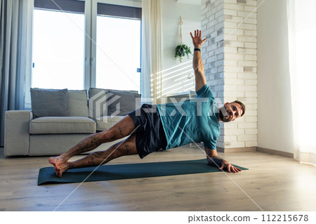 Handsome man doing yoga, stretching, resting after home workout, New Year's resolutions, exercising as healthy lifestyle and selfcare. 112215678