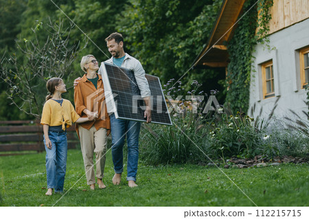 Father mother and daughter walking in garden with solar panel. Solar energy and sustainable lifestyle of young family. 112215715