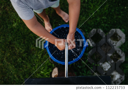 Boy washing his hands with water from a well. Well with a pump for outdoor washing in garden. Boy washing his hands with water from a well. Well with a pump for outdoor washing in garden. 112215733