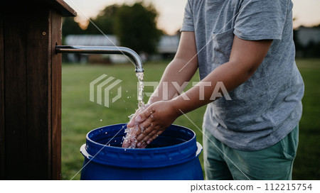 Boy washing his hands with water from a well. Well with a pump for outdoor washing in garden. 112215754