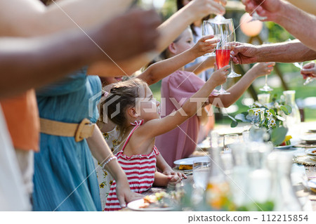 Family clinking glasses at summer garden party, kids clinking with nonalcoholic drink, lemonade. Celebratory toast at table. Big family garden bbq. Family clinking glasses at summer garden party, kids clinking with nonalcoholic drink, lemonade. Celebratory toast at table. Big family garden bbq. 112215854