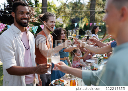 Friends clinking glasses at summer garden party. Celebratory toast at the table. 112215855
