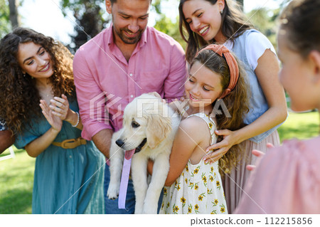 Beautiful birthday girl received puppy as birthday gift. Garden birthday party for young girl. 112215856