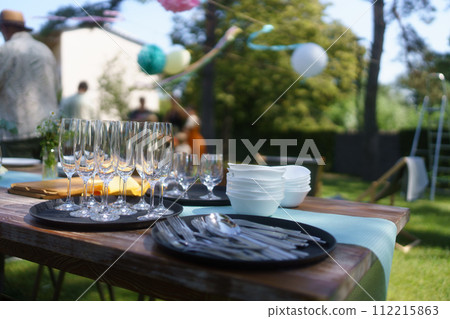 Close up shot of empty wine glasses, cutlery and utensils at summer garden party. Close up shot of empty wine glasses, cutlery and utensils at summer garden party. 112215863
