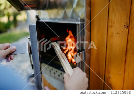 Unrecognizable woman putting piece of wood in outdoor hot tub. Close-up. 112215998