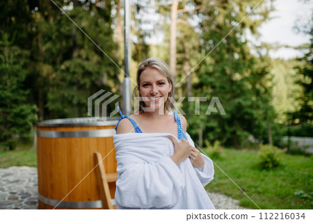 Young woman preapring to get into woodfired hot bath outdoors. Summer holidays in the mountains, hot water treatments and thermal spa concept. Young woman preapring to get into woodfired hot bath outdoors. Summer holidays in the mountains, hot water treatments and thermal spa concept. 112216034
