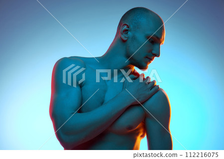 Handsome young bald man with relief, shirtless sportive body, posing against blue studio background in neon light Handsome young bald man with relief, shirtless sportive body, posing against blue studio background in neon light 112216075
