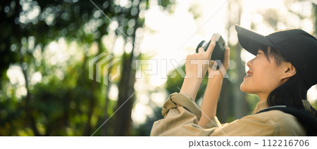 Panoramic photo of smiling female traveller taking photo with camera in nature. Holiday, travel and lifestyle concept 112216706