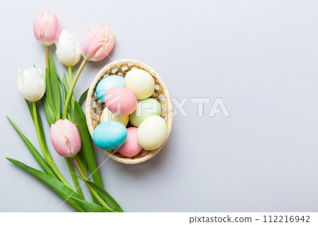 Happy Easter composition. Easter eggs in basket on colored table with yellow Tulips. Natural dyed colorful eggs background top view with copy space Happy Easter composition. Easter eggs in basket on colored table with yellow Tulips. Natural dyed colorful eggs background top view with copy space 112216942