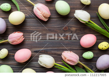 Happy Easter composition. Easter eggs on colored table with yellow Tulips. Natural dyed colorful eggs background top view with copy space 112217005