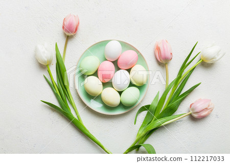 Happy Easter composition. Easter eggs in basket on colored table with yellow Tulips. Natural dyed colorful eggs background top view with copy space 112217033