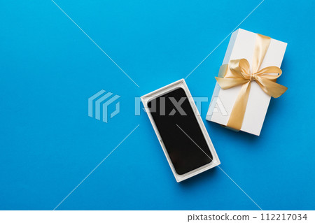Opened gift box with gold ribbon and smartphone on color background, top view. Blank open box packaging mockup , Template for your design - branding mockup 112217034