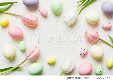 Happy Easter composition. Easter eggs on colored table with yellow Tulips. Natural dyed colorful eggs background top view with copy space 112217035