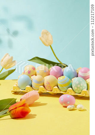 Easter joy captured in picturesque frame. The colorful and patterned eggs are arranged in a blister decorated with tulips on pastel color background. Idea for Easter decoration Easter joy captured in picturesque frame. The colorful and patterned eggs are arranged in a blister decorated with tulips on pastel color background. Idea for Easter decoration 112217109