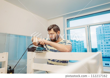 man rubs wooden child bed with power sander or grinder removing old paint man rubs wooden child bed with power sander or grinder removing old paint 112217162