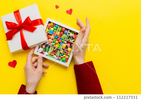 Female hands with delicious candies in box on color background 112217331