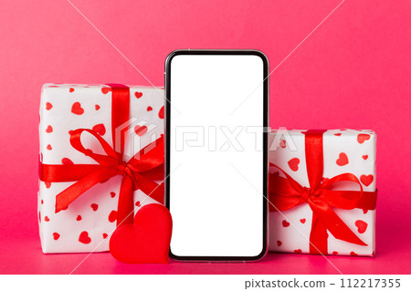 mobile phone with blank screen on colored background with hearts, calendar and gift box, valentine day concept perspertive view flat lay mobile phone with blank screen on colored background with hearts, calendar and gift box, valentine day concept perspertive view flat lay 112217355