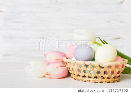 Happy Easter composition. Easter eggs in basket on colored table with yellow Tulips. Natural dyed colorful eggs background with copy space Happy Easter composition. Easter eggs in basket on colored table with yellow Tulips. Natural dyed colorful eggs background with copy space 112217390