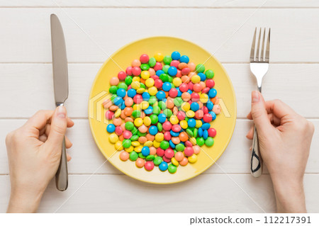 the girl holds cutlery in her hands and eats sweets in a plate. Health and obesity concept, top view on colored background 112217391