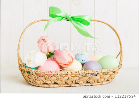 Happy Easter composition. Easter eggs in basket on colored table with yellow Tulips. Natural dyed colorful eggs background with copy space 112217554
