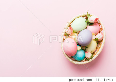 Happy Easter. Easter eggs in basket on colored table with yellow roses. Natural dyed colorful eggs background top view with copy space Happy Easter. Easter eggs in basket on colored table with yellow roses. Natural dyed colorful eggs background top view with copy space 112217604