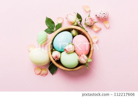 Happy Easter. Easter eggs in basket on colored table with yellow roses. Natural dyed colorful eggs background top view with copy space 112217606