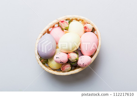 Happy Easter. Easter eggs in basket on colored table with yellow roses. Natural dyed colorful eggs background top view with copy space 112217610