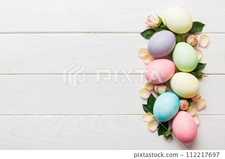 Happy Easter. Easter eggs on colored table with yellow roses. Natural dyed colorful eggs background top view with copy space Happy Easter. Easter eggs on colored table with yellow roses. Natural dyed colorful eggs background top view with copy space 112217697