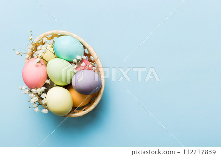 Happy Easter composition. Easter eggs in basket on colored table with gypsophila. Natural dyed colorful eggs background top view with copy space 112217839
