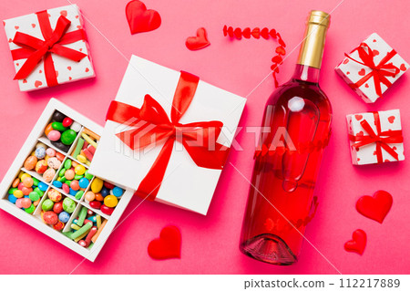 Bottle of red wine on colored background for Valentine Day with gift and chocolate. Heart shaped with gift box of chocolates top view with copy space 112217889