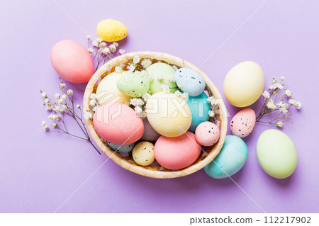 Happy Easter composition. Easter eggs in basket on colored table with gypsophila. Natural dyed colorful eggs background top view with copy space 112217902