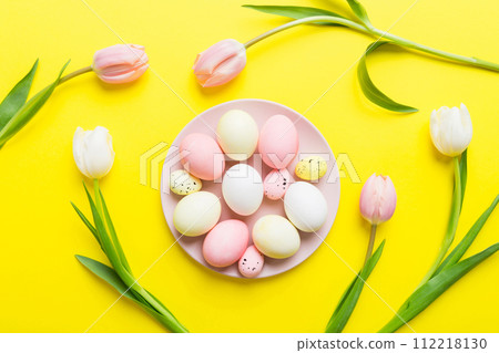 Happy Easter composition. Easter eggs in basket on colored table with yellow Tulips. Natural dyed colorful eggs background top view with copy space Happy Easter composition. Easter eggs in basket on colored table with yellow Tulips. Natural dyed colorful eggs background top view with copy space 112218130