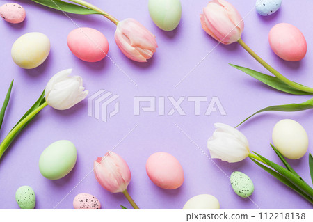 Happy Easter composition. Easter eggs on colored table with yellow Tulips. Natural dyed colorful eggs background top view with copy space Happy Easter composition. Easter eggs on colored table with yellow Tulips. Natural dyed colorful eggs background top view with copy space 112218138