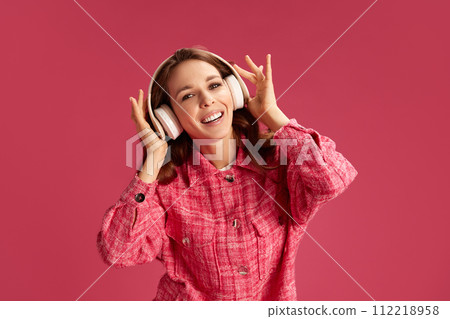 Happy, beautiful, smiling young woman in checkered shirt, smiling. listening to music in headphones against pink studio background 112218958