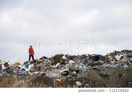 Activist standing on landfill, on large pile of waste with dark clouds above. Environmental concept and eco activism. Activist standing on landfill, on large pile of waste with dark clouds above. Environmental concept and eco activism. 112218982