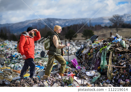 Couple of hikers walking across landfill, large pile of waste, environmental concept and eco activism. 112219014