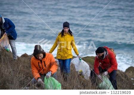Group of activists picking up litter along riverbank. River clean up. Environmental pollution, eco activism. and plogging concept. Group of activists picking up litter along riverbank. River clean up. Environmental pollution, eco activism. and plogging concept. 112219020