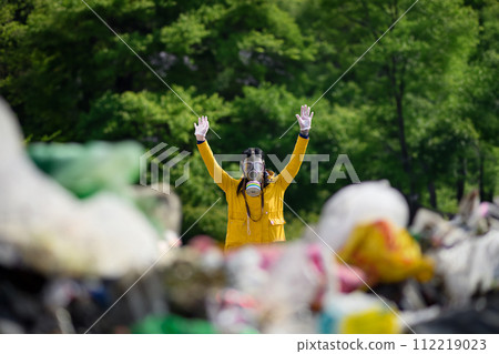 Activist with gas mask holding hands up, standing on landfill, large pile of waste, environmental concept and eco activism. 112219023