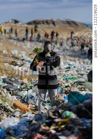 Man with gas mask and plant on landfill standing on landfill, large pile of waste, environmental concept and eco activism. Man with gas mask and plant on landfill standing on landfill, large pile of waste, environmental concept and eco activism. 112219029