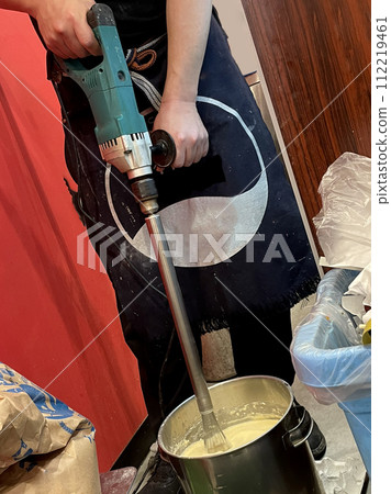 Hand of an employee whipping powdered ingredients with an electric whisk at a restaurant Hand of an employee whipping powdered ingredients with an electric whisk at a restaurant 112219461