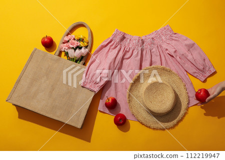 Female blouse, hat, flowers in bag and apples in hand on yellow background, top view 112219947