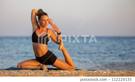 Outdoor yoga practicing at the beach. Fitness woman doing mermaid pose Outdoor yoga practicing at the beach. Fitness woman doing mermaid pose 112220135