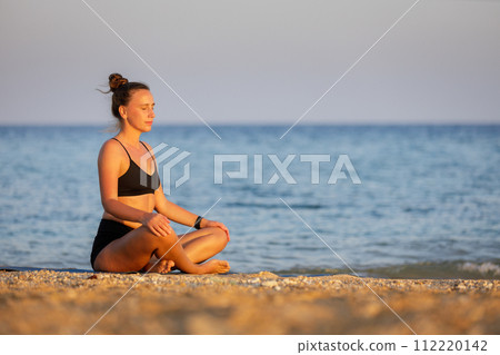 Fitness woman breathing and meditating near the sea at sunset Fitness woman breathing and meditating near the sea at sunset 112220142