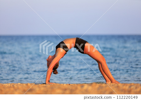 Outdoor yoga practicing at the beach. Fitness woman doing wheal pose 112220149