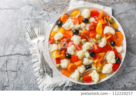 Delicious cauliflower salad with pickled vegetables, olives and anchovies close-up on a plate. Horizontal top view 112220257