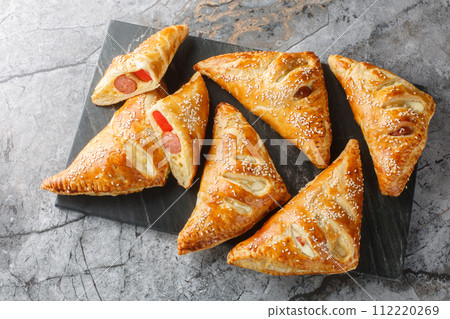 Puff pastry Pigs in a blanket pies with sausage, cheese, sesame and pepper close-up on a marble board. Horizontal top view 112220269