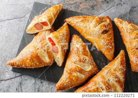Delicious puff pastry pies with sausage, cheese, sesame and pepper close-up on a marble board. Horizontal top view Delicious puff pastry pies with sausage, cheese, sesame and pepper close-up on a marble board. Horizontal top view 112220271